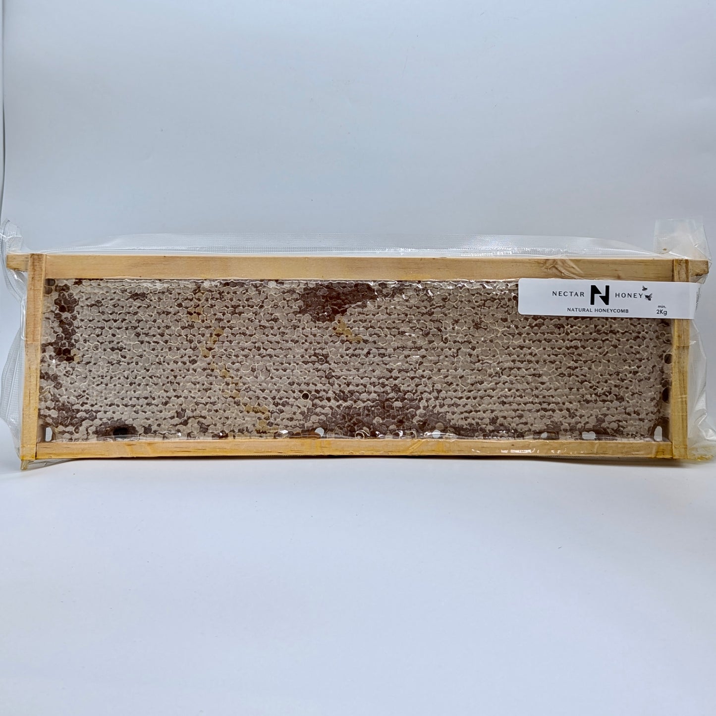 A timber frame of raw honeycomb with beeswax cells, sealed in a vacuum-sealed plastic packaging with a white label on top.
