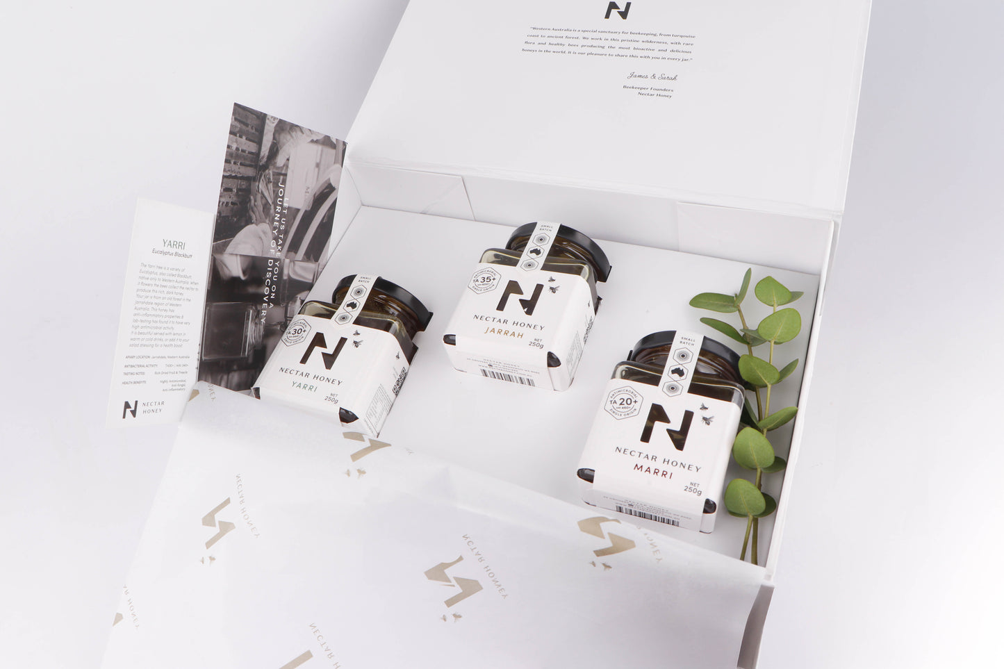 Three jars with labels on a white surface with a magazine or newspaper in the background.