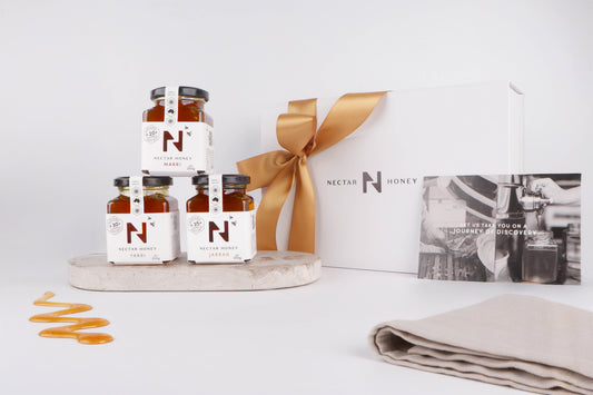 Jars of Nectar Honey on a white surface with a gift box and ribbon.